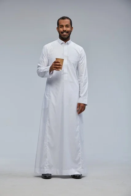رجل سعودي بالثوب التقليدي يحمل كوب قهوة في استوديو