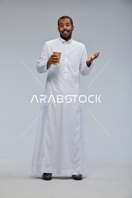 رجل سعودي مبتسم يحمل كوب قهوة بالزي التقليدي