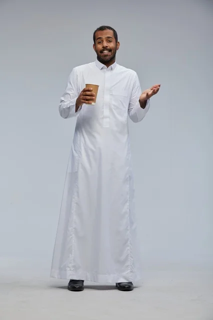 رجل سعودي مبتسم يحمل كوب قهوة بالزي التقليدي
