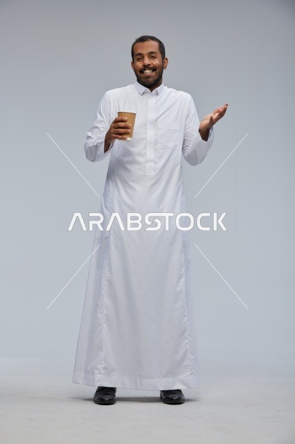 رجل سعودي بالثوب الأبيض التقليدي يحمل كوب قهوة
