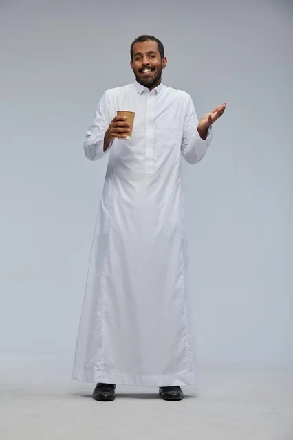 رجل سعودي بالثوب الأبيض التقليدي يحمل كوب قهوة