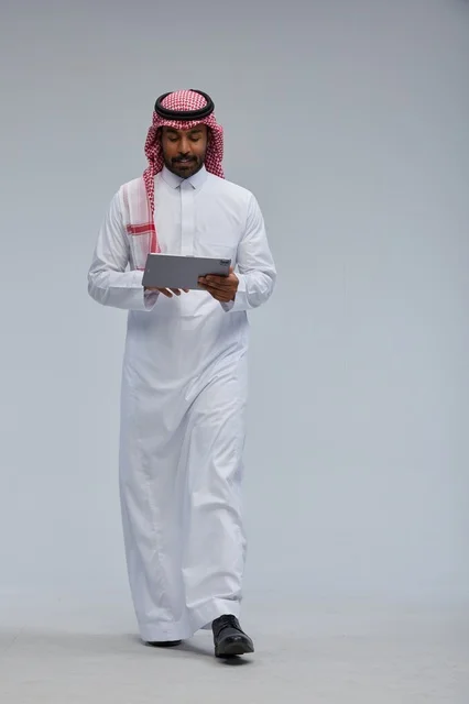 Saudi Man in Thobe Using Tablet on Gray Background