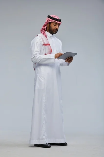 رجل سعودي بالزي التقليدي يستخدم جهاز لوحي