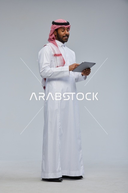 رجل سعودي يستخدم جهازًا لوحيًا بالزي التقليدي
