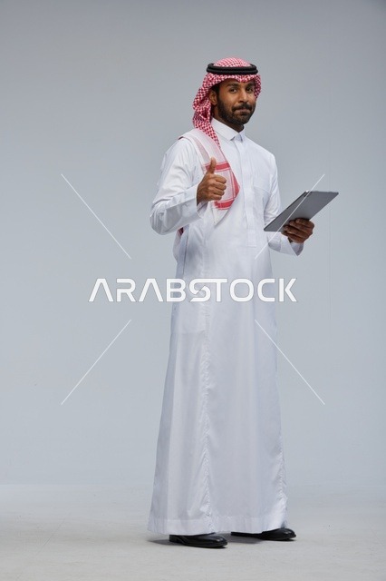 رجل سعودي يحمل جهازا لوحيا مع إشارة الإعجاب