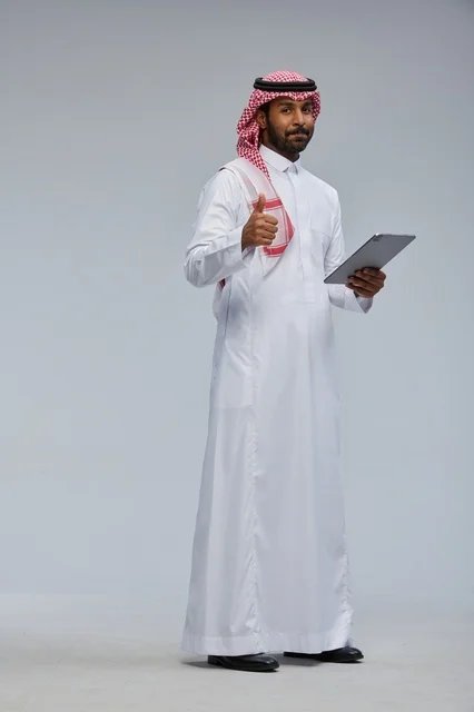 رجل سعودي يحمل جهازا لوحيا مع إشارة الإعجاب