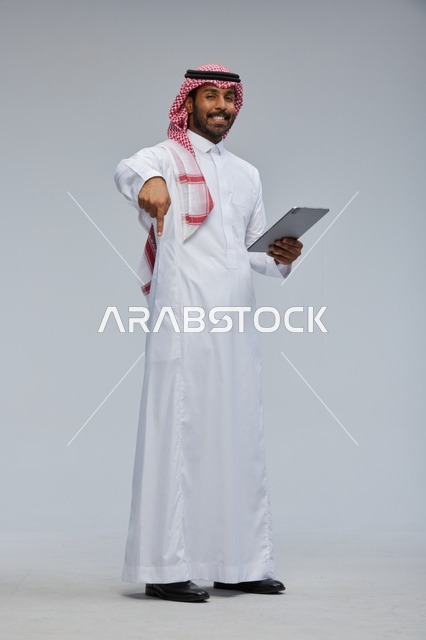 رجل سعودي بالزي التقليدي يحمل جهازاً لوحياً ويشير