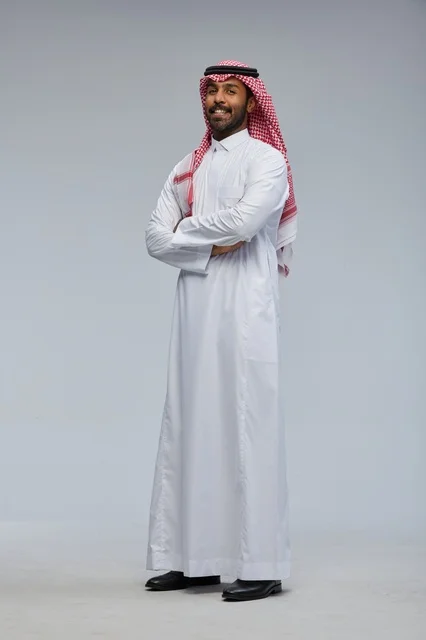 رجل سعودي مبتسم بالزي التقليدي بذراعين متقاطعتين