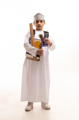 طالب عماني بالزي التقليدي يحمل أدوات مدرسية