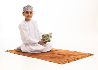Omani Boy Holding Holy Quran on Prayer Mat Studio Background