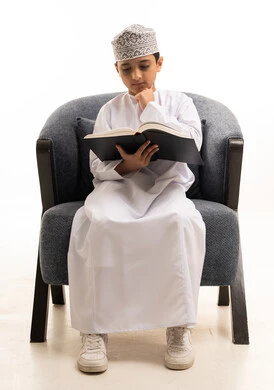طفل عماني يقرأ كتاباً بالزي التقليدي العماني