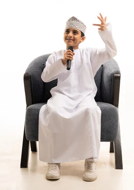 طفل عماني باللباس التقليدي يمسك بميكروفون