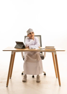 Omani Boy in Traditional Dress Thinking at Desk