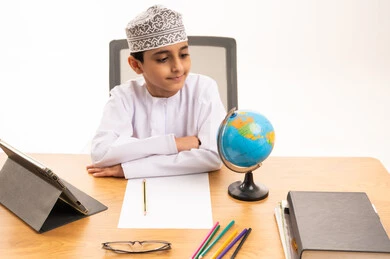 Omani Boy Wearing Traditional Clothes Studying with Globe
