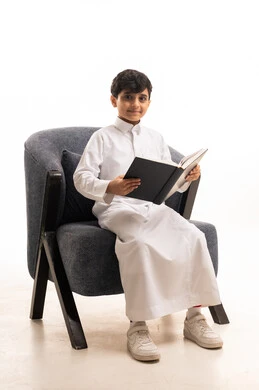 طفل سعودي بالثوب الأبيض يقرأ كتابا