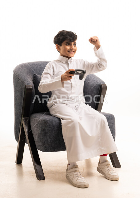 طفل سعودي يرتدي الثوب الأبيض ويلعب ألعاب الفيديو فائزاً