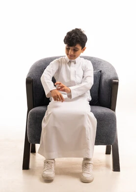 Saudi Boy in Traditional White Thobe Sitting on Armchair
