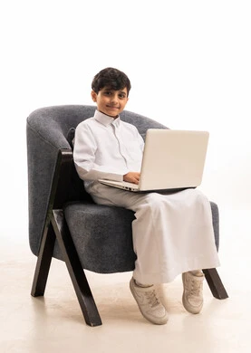 Saudi Boy in Traditional Thobe Using Laptop in Studio