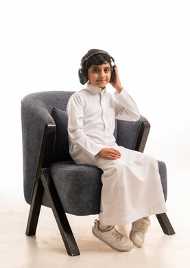 Saudi Boy in Thobe Using Headphones in Studio