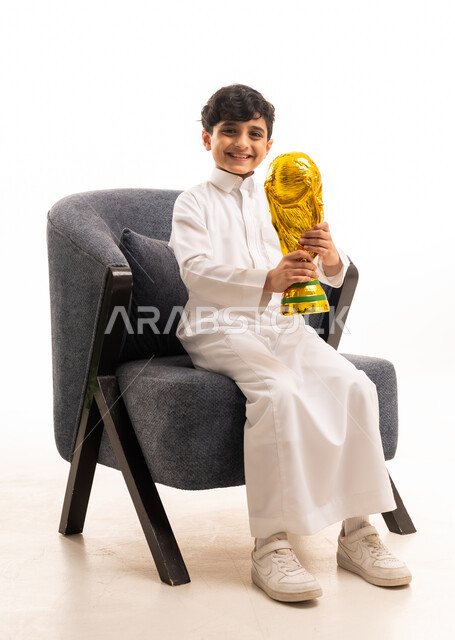 طفل سعودي بالثوب التقليدي يحمل كأس العالم الذهبية
