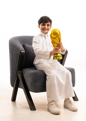 طفل سعودي بالثوب التقليدي يحمل كأس العالم الذهبية