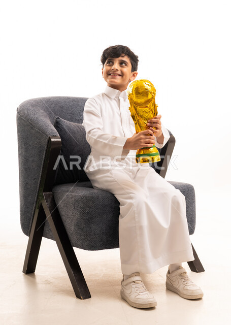 طفل سعودي بالثوب التقليدي يحمل كأس العالم الذهبي