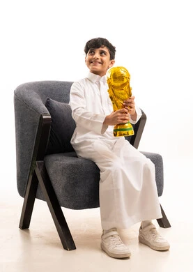طفل سعودي بالثوب التقليدي يحمل كأس العالم الذهبي