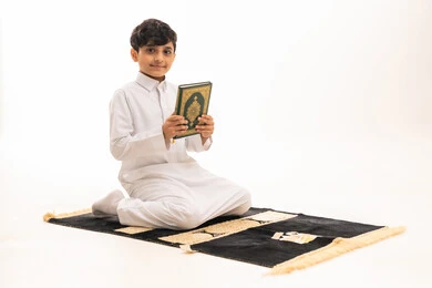 Saudi Boy in White Thobe Holding Quran on Prayer Mat