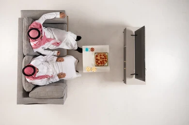 رجال سعوديون بالزي التقليدي يشاهدون التلفاز مع البيتزا