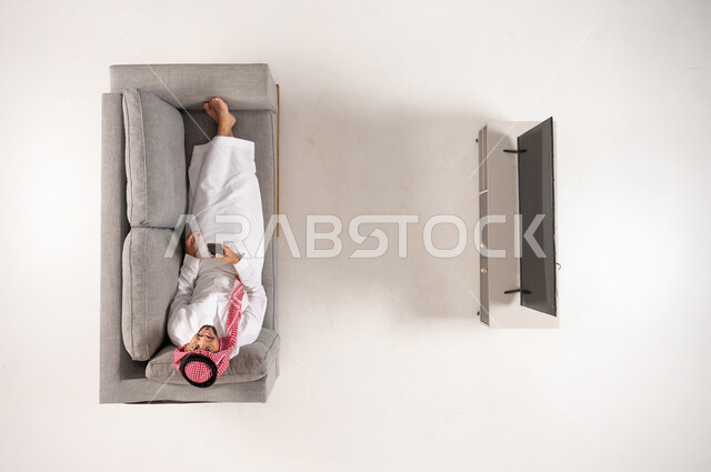 رجل سعودي يستخدم الهاتف على الأريكة منظر علوي بسيط