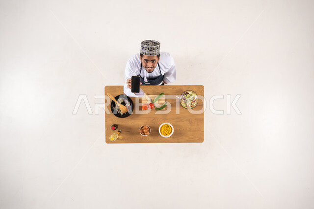 رجل عماني يطهو الطعام مع هاتف ذكي منظور علوي استوديو