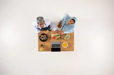 رجل وامرأة من عمان يطبخان مع كمبيوتر محمول لقطة علوية
