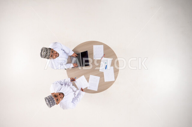 رجال عمانيون يعملون على طاولة بمنظور علوي