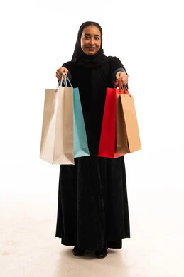 امرأة سعودية تحمل حقائب تسوق ملونة أمام خلفية بيضاء