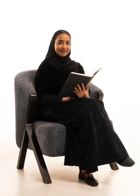 امرأة سعودية بالعباءة تقرأ كتاباً في الاستوديو
