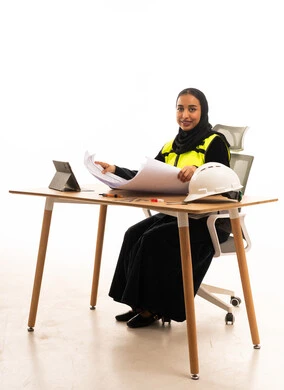 مهندسة سعودية مع مخططات هندسية وخوذة أمان