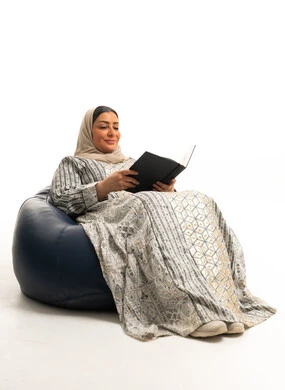 امرأة سعودية ترتدي جلابية تقليدية تقرأ على كرسي مريح
