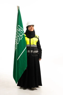 مهندسة سعودية مع العلم بملابس السلامة والخوذة