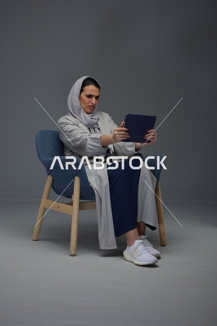 امرأة سعودية تستخدم جهازاً لوحياً بتعبير وجه مرتبك