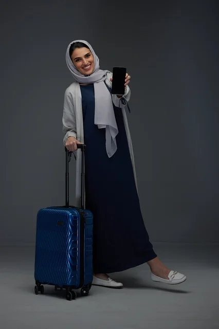 امرأة سعودية مع حقيبة سفر وهاتف ذكي