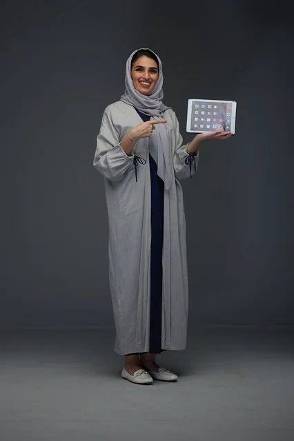 امرأة سعودية في استوديو تحمل جهازاً لوحياً وتشير إليه