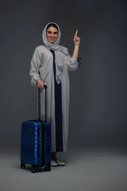 امرأة سعودية مسافرة مع حقيبة زرقاء تشير للأعلى