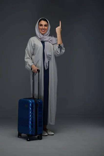 Saudi Woman Traveler With Blue Suitcase Pointing Up