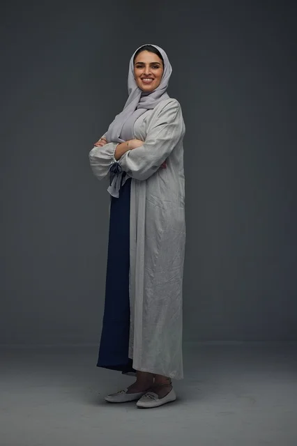 امرأة سعودية بعباءة رمادية تقف في الاستوديو