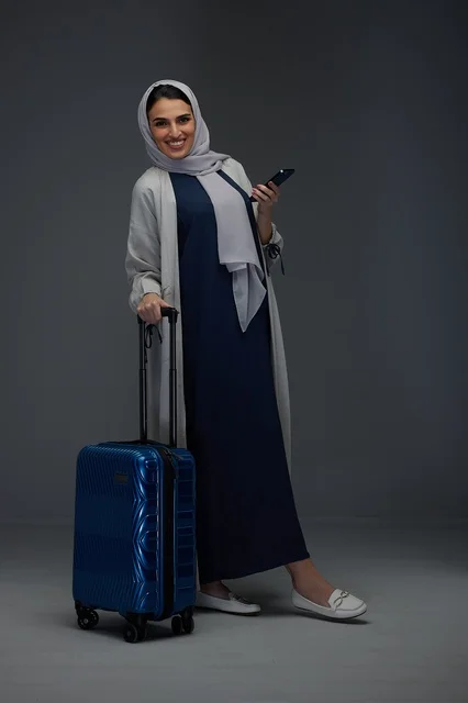 امرأة سعودية مسافرة مع حقيبة سفر زرقاء وهاتف ذكي