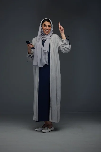 امرأة سعودية تحمل هاتفاً ذكياً وتشير للأعلى في استوديو