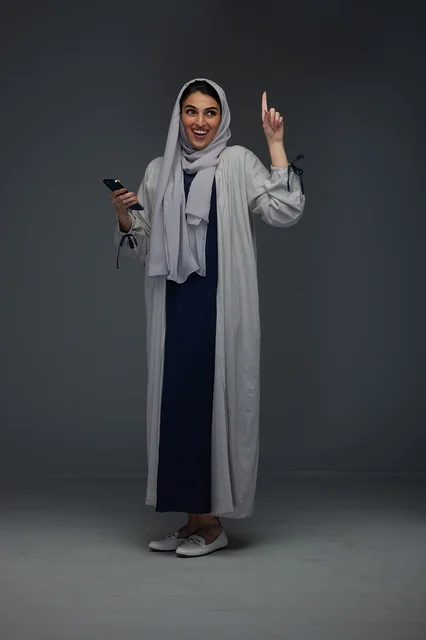 امرأة سعودية تشير للأعلى وتحمل هاتفاً ذكياً في الاستوديو