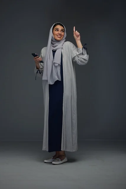 امرأة سعودية تشير للأعلى وتحمل هاتفاً ذكياً في استوديو