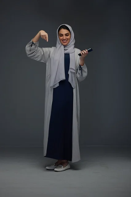 امرأة سعودية تحمل هاتفاً ذكياً في استوديو بخلفية رمادية