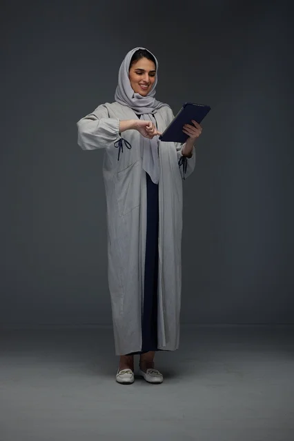امرأة سعودية بعباءة رمادية تستخدم جهاز لوحي في استوديو